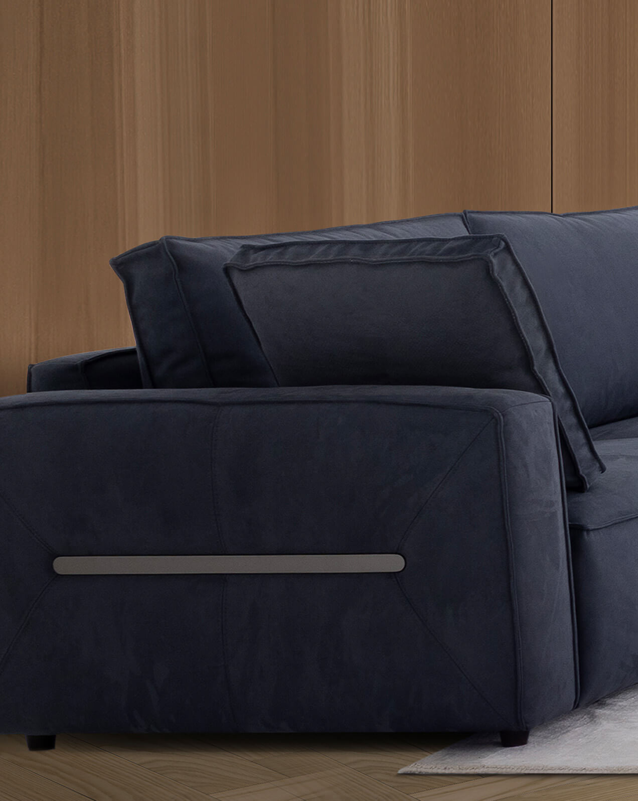 Close-up view of the armrest and back cushions of a dark navy sectional sofa with a sleek metal accent on the side, set against a light wooden wall and a neutral rug.